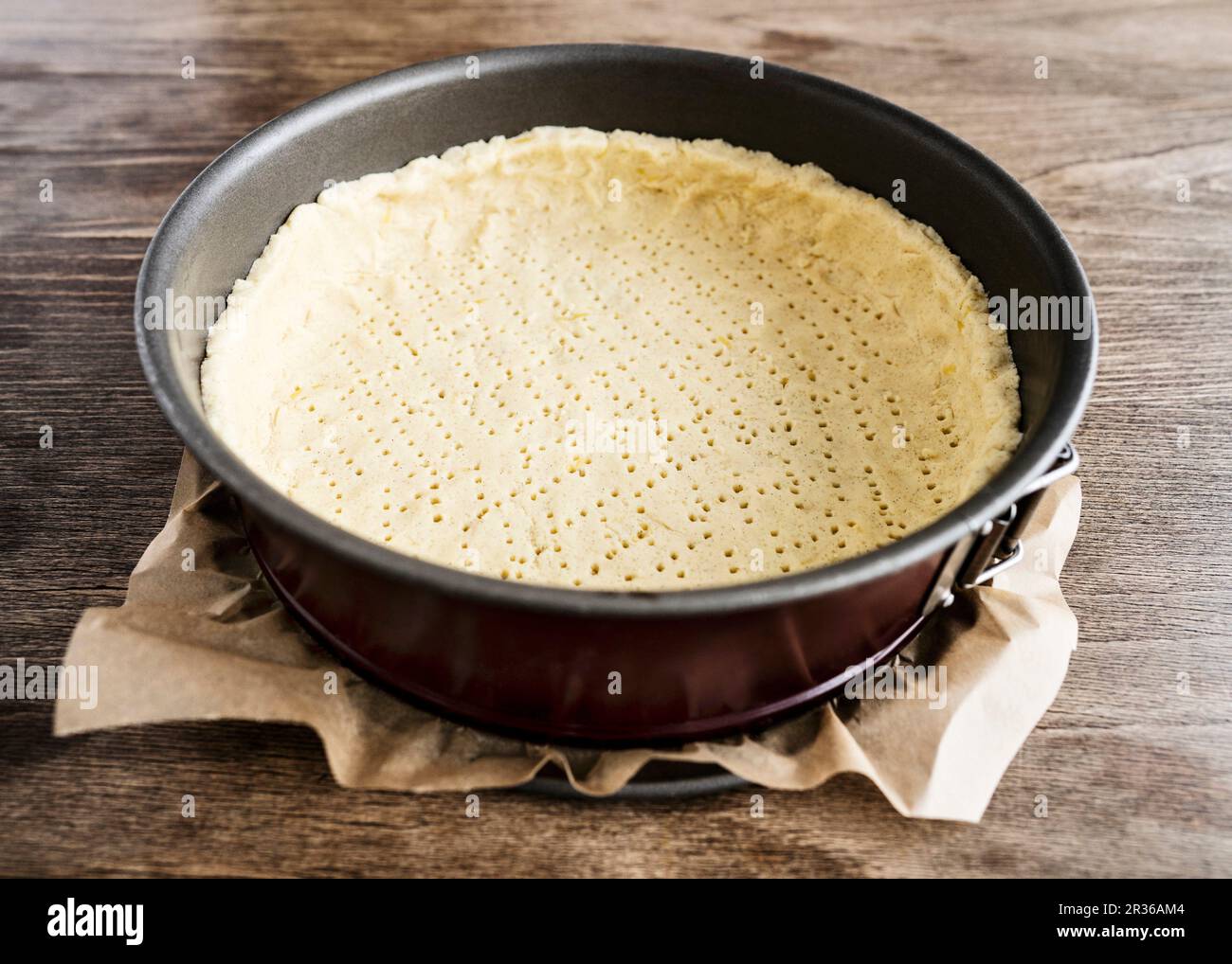Mürbteig Gebäck in einem dunklen Rot Springform mit Backpapier auf einem Holztisch Stockfoto