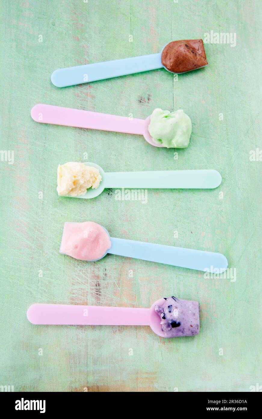 Verschiedene Eissorten auf Eislöffeln: Vanille, Erdbeere, Schokolade, Heidelbeere und Minze Stockfoto