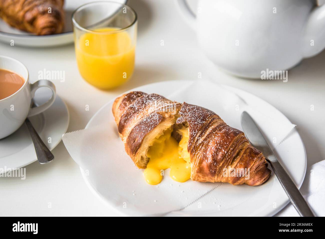 Ein mit gesalzenem Eigelb gefülltes Croissant auf einem Teller mit Tee und Orangensaft Stockfoto