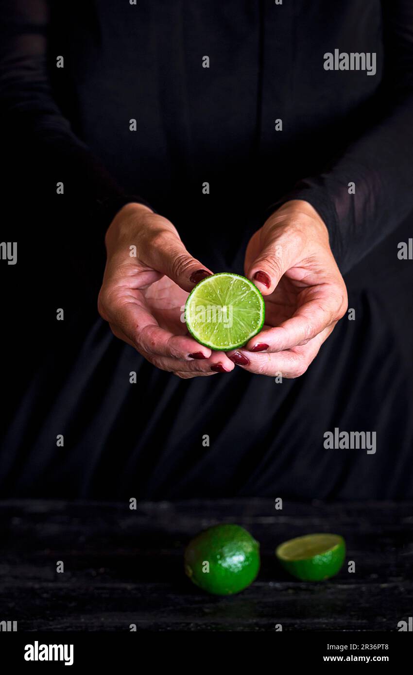 Eine halbe Limette in die Hände einer Frau vor einem schwarzen Hintergrund Stockfoto