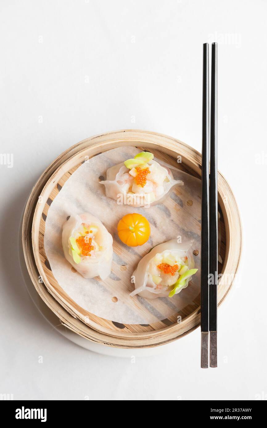 Gedünstete chinesische Teigtaschen mit Garnelen und Fischrogen in Bambus-Dampfkorb mit Essstäbchen Stockfoto