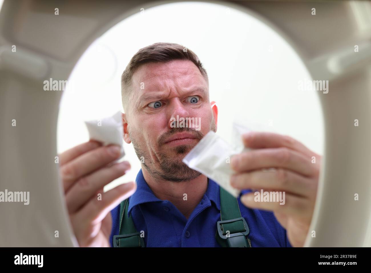 Ein unrasierter Mann steht über der Toilettenschüssel und hält Betäubungstüten Stockfoto