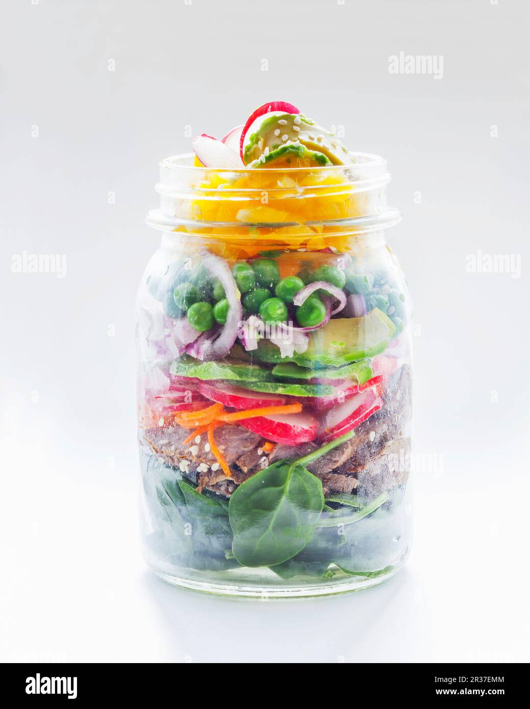 Gemüsesalat mit Erbsen, Avocado, Radieschen, Brot und Spinat in einem Glasgefäß Stockfoto