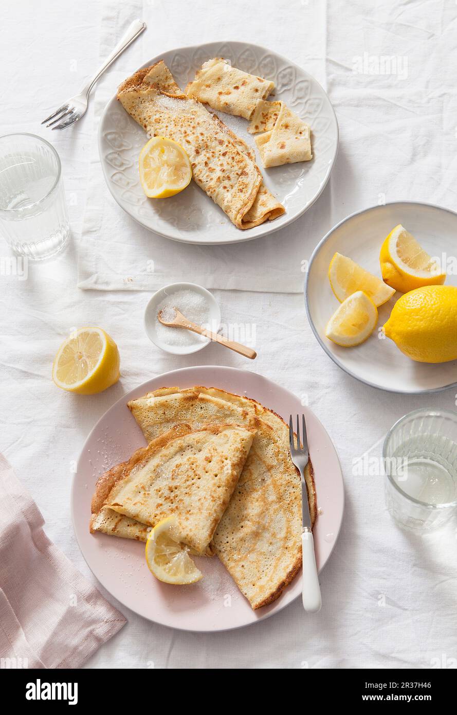 Zwei Platten von gefaltet und gerollt Pfannkuchen mit zitronekeile serviert auf weißem Leinen gedeckten Tisch und Wasser Gläser Stockfoto