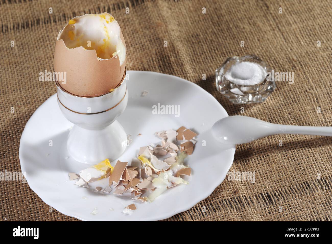 Weich gekochtes Ei in einem Keramikeibecher mit flüssigem gelbem Eigelb und passendem weißem Keramiklöffel Stockfoto