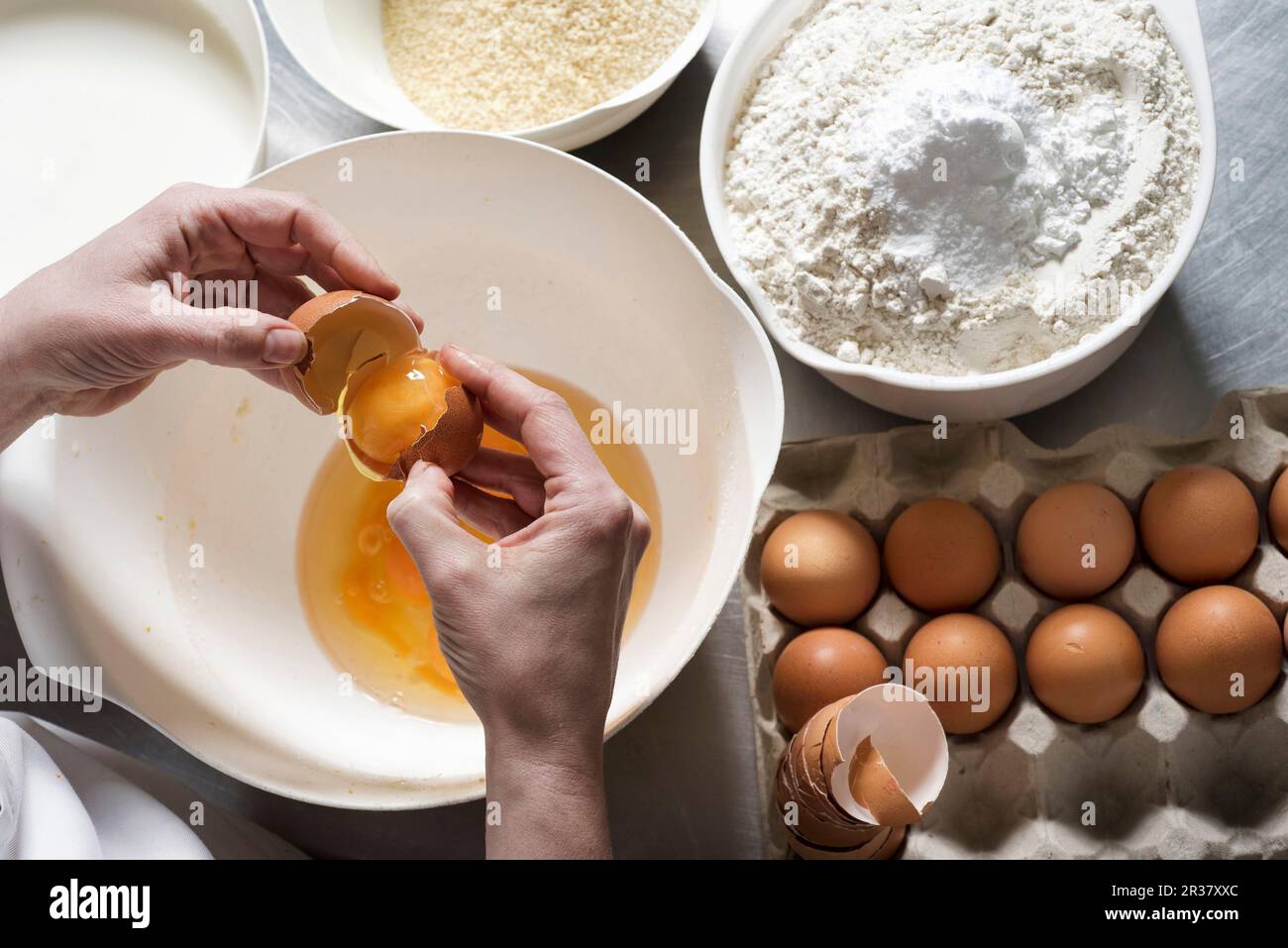 Hände zerbrechen Eier über einer Schüssel mit Mandelmehl und regelmäßigem Mehl mit Backpulver daneben Stockfoto