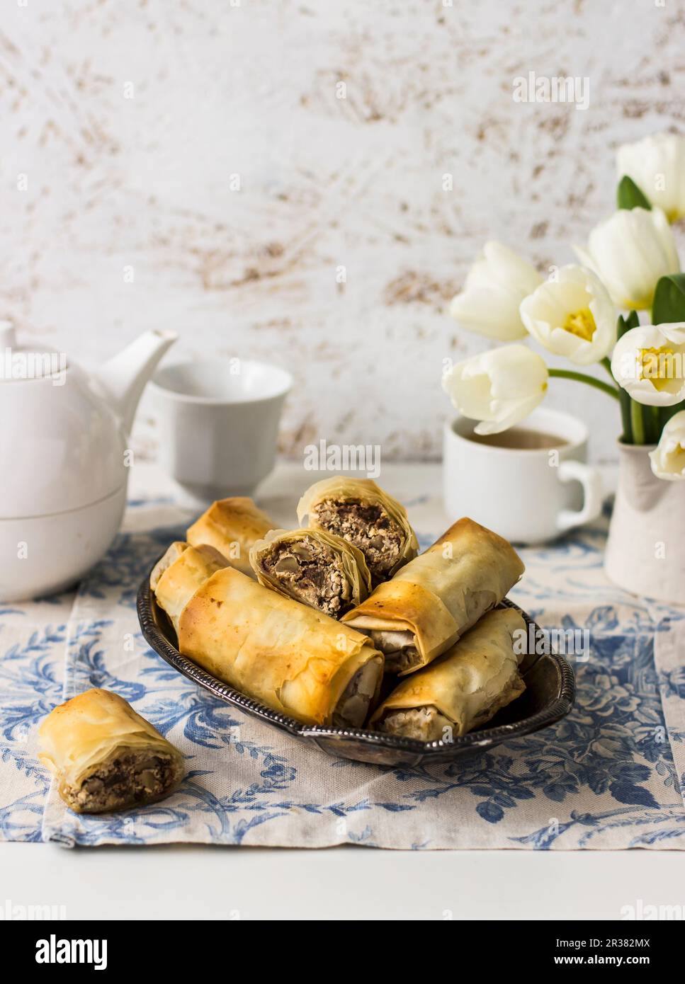 Filo Brötchen mit Manouri-Käse, Walnüssen, Rosinen und Minze; Tee, Weiße Tulpen Stockfoto