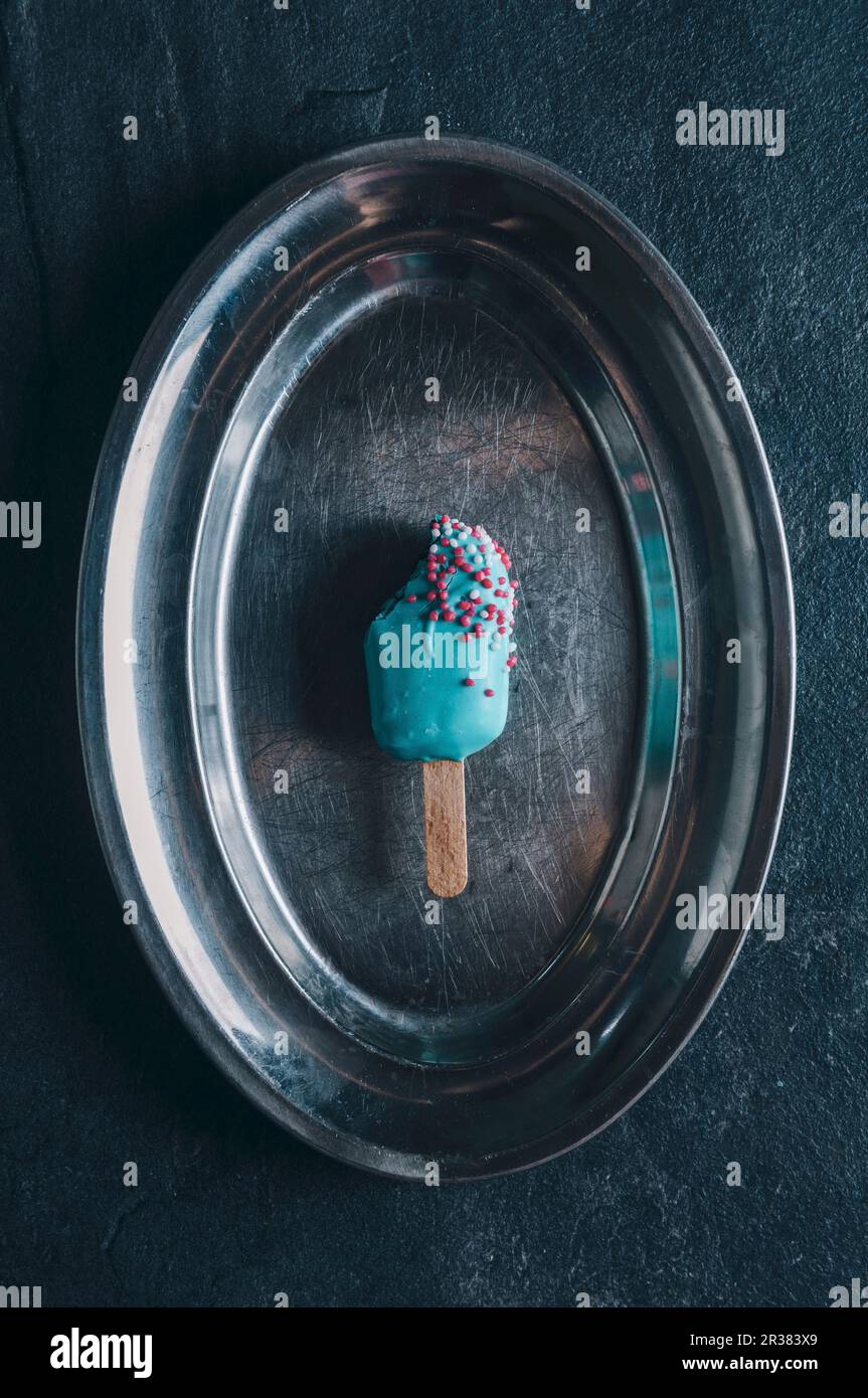 Ein Kuchen-Pop in Form eines Eislollys mit bunten Glasuren auf einem silbernen Tablett Stockfoto