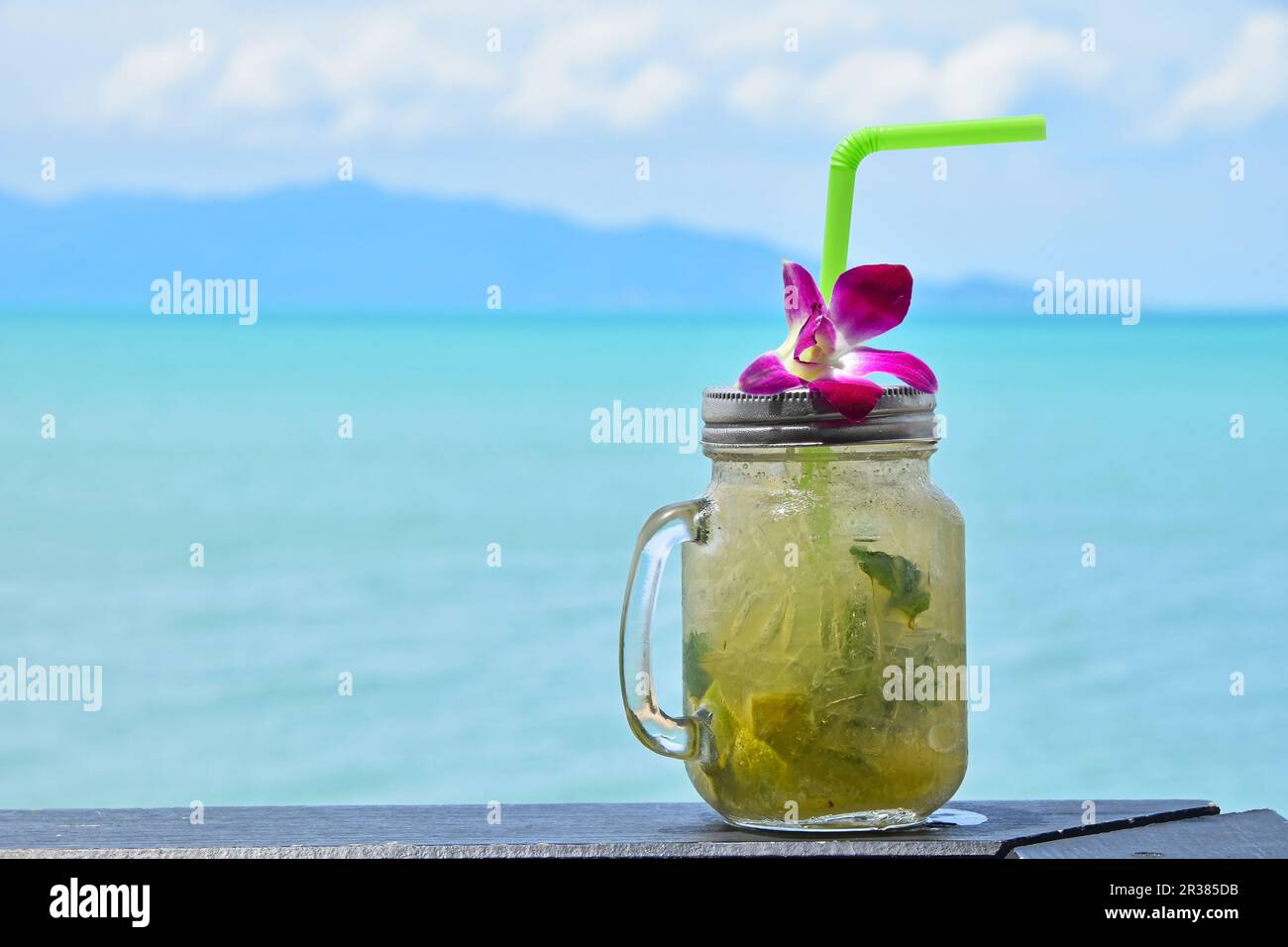 Großes Glas Mojito mit orchideenblüte am Strand Stockfoto