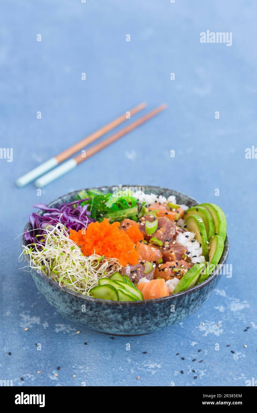 Eine Poke-Schüssel mit Wakame-Algen, Thunfisch, Sushi-Reis, Lachs, Luzerne, Rotkohl, Sesamsamen, Gurkenscheiben, Frühlingszwiebeln, Avocado, Und an Stockfoto