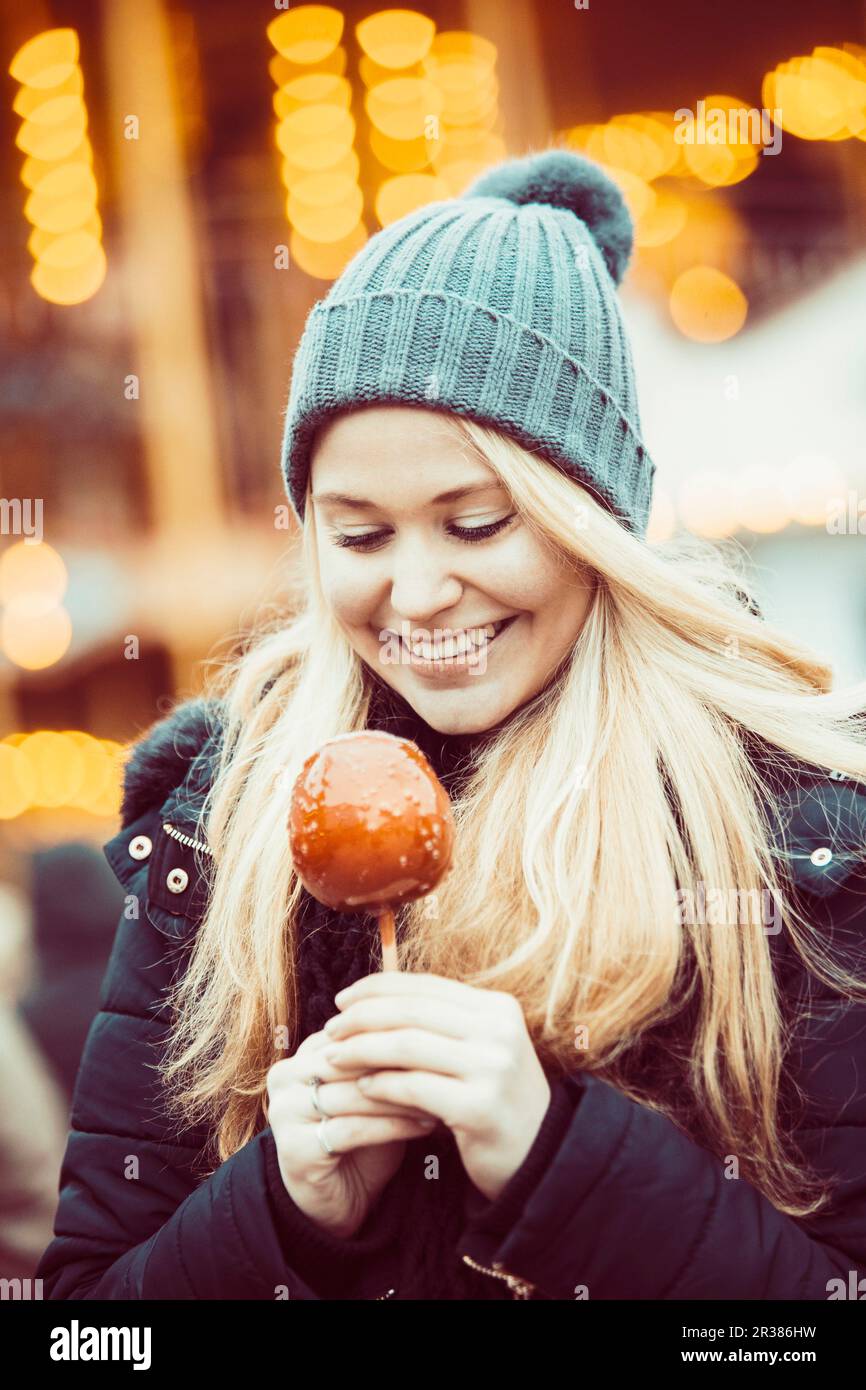 Eine junge Frau, gekleidet für den Winter, mit einem Toffee-Apfel auf einem Weihnachtsmarkt Stockfoto