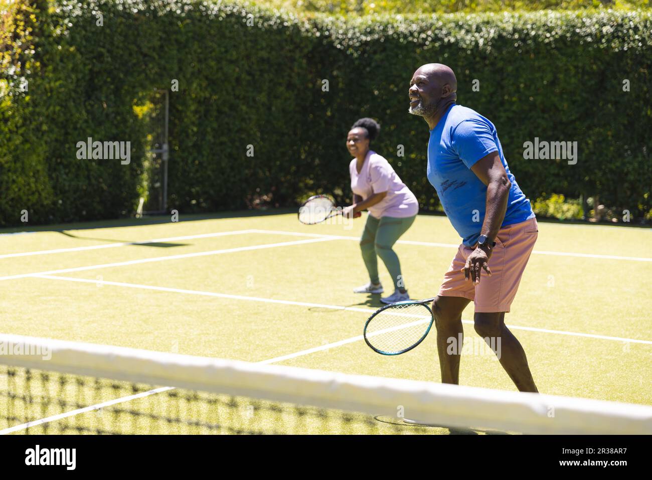 Glückliches Senior-afroamerikanisches Paar, das auf einem sonnigen Tennisplatz Tennis-Doppel spielt, Kopierraum Stockfoto