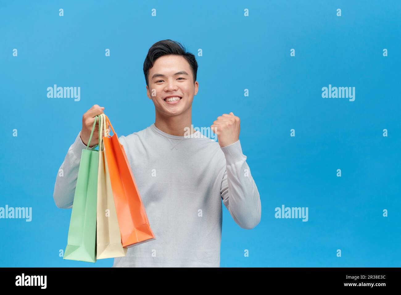 Junger asiatischer Mann, super glücklich, Einkaufstüten in der Hand zu haben, isoliert auf blauem Hintergrund. Stockfoto
