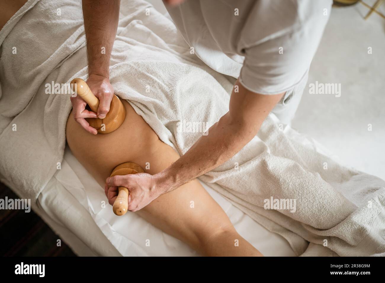 Unbekannte weiße Frau, die eine madero-Therapie-Massage gegen Cellulite-Behandlung durch einen professionellen Therapeuten mit Holzwerkzeugen in den Händen im Studio oder in der sa erhalten hat Stockfoto