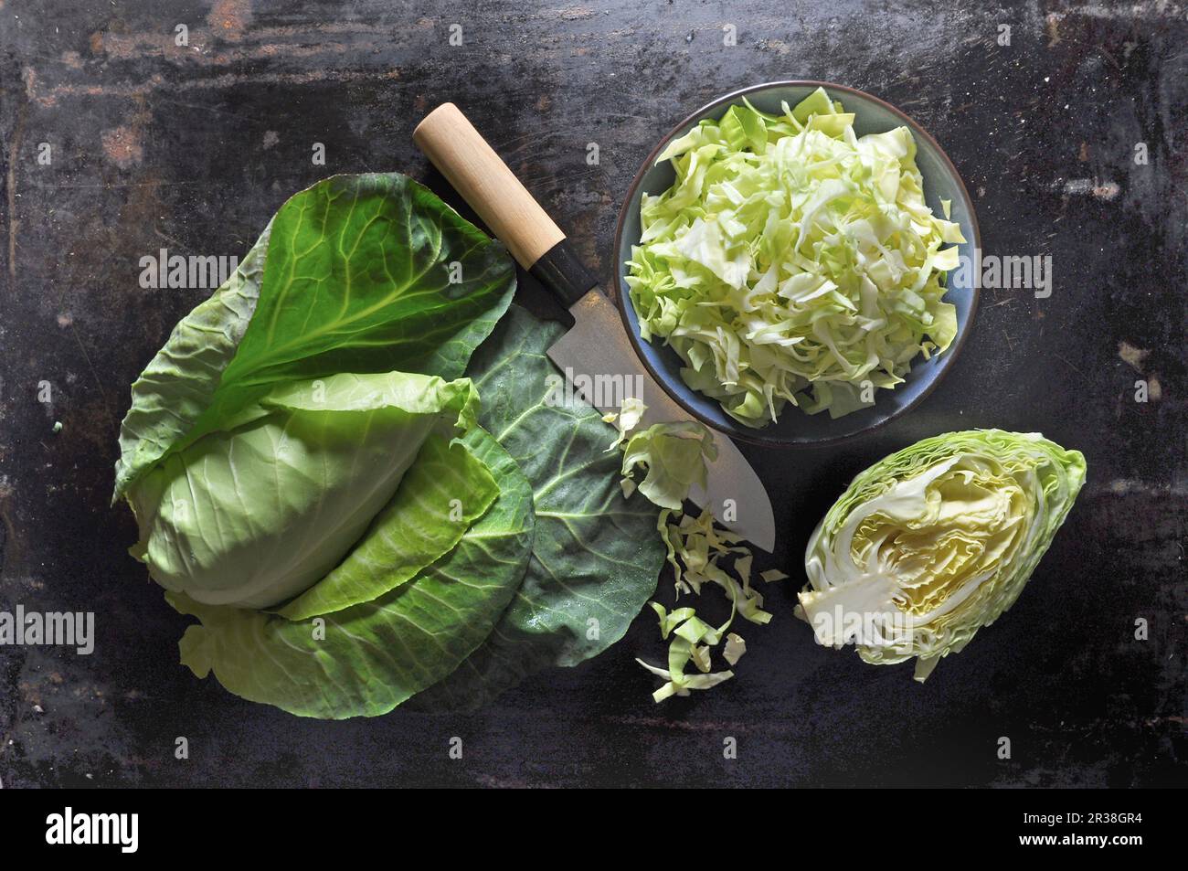 Spitzkohl, ganz, halbiert und in Scheiben geschnitten, in eine keramische Schüssel mit einem Messer auf einem schwarzen Backblech Stockfoto