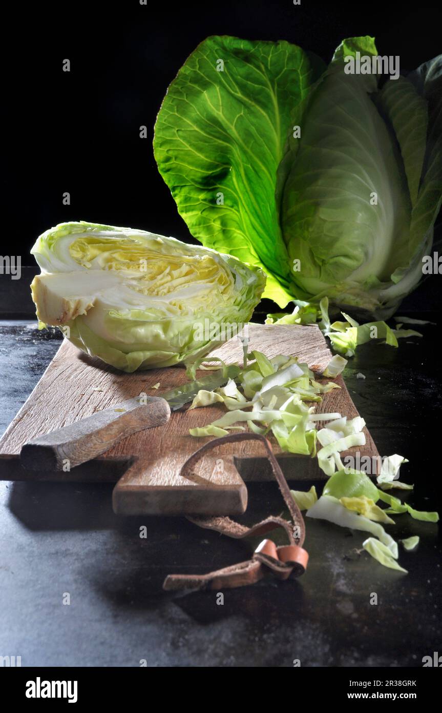 Spitzkohl, ganz, halbiert und in Scheiben geschnitten, auf einem Schneidebrett mit Messer auf einem schwarzen Backblech Stockfoto