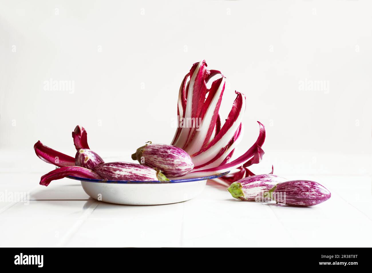 Uber eine Anordnung von Trevisio und kleinen Auberginen auf einer alten Schmelzplatte Stockfoto