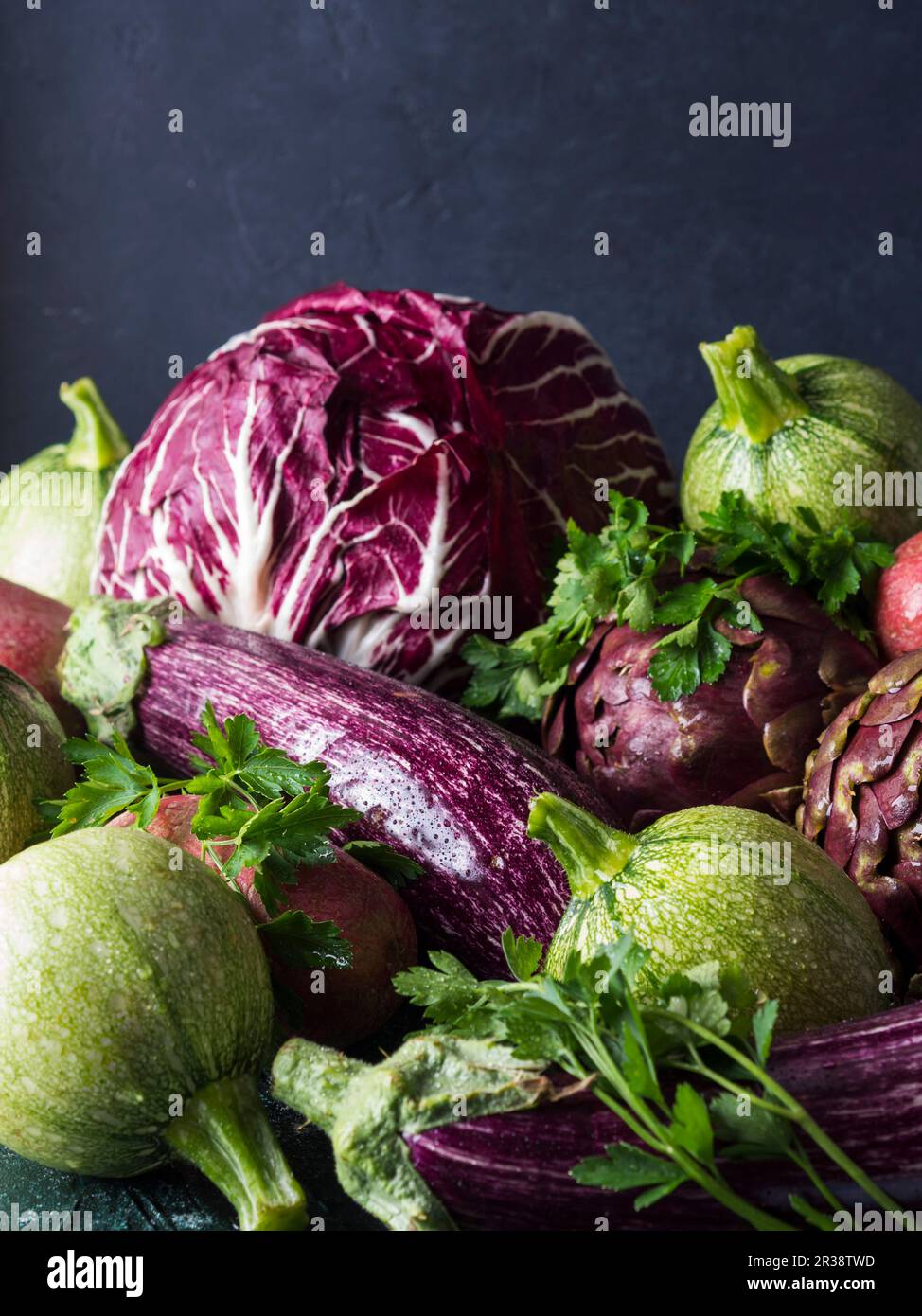 Auswahl an rohem grünen und violetten Gemüse - Zichorie, rote Kartoffeln, Zucchini, Artischocken und Auberginen - auf schwarzem Hintergrund Stockfoto