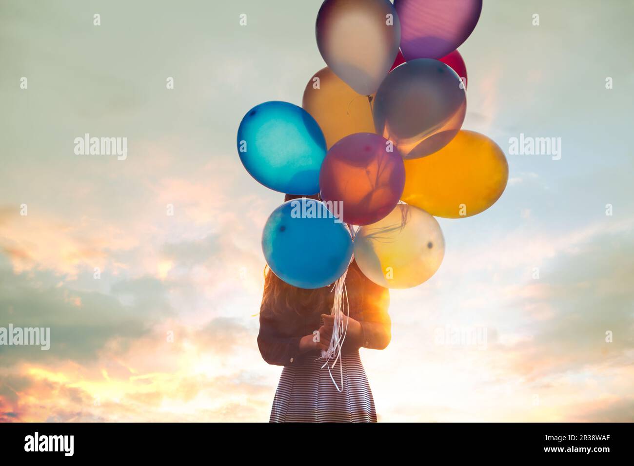 Junges Mädchen hält ein Bündel Luftballons vor dem Gesicht Stockfoto