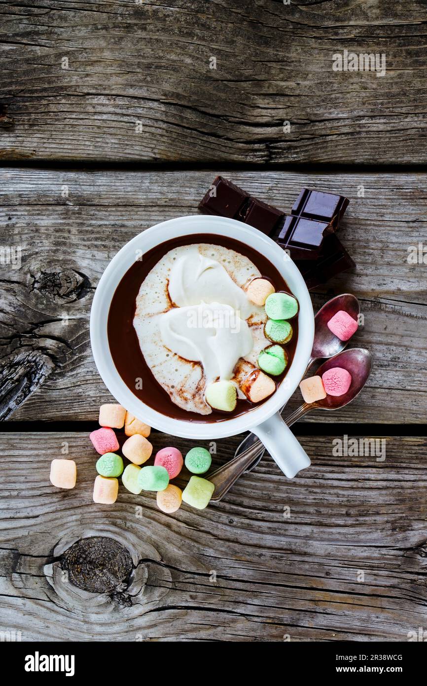 Nahaufnahme von heißer Schokolade in weißem Keramikbecher mit Schlagsahne und Marshmallows auf rustikalem Holzhintergrund Stockfoto
