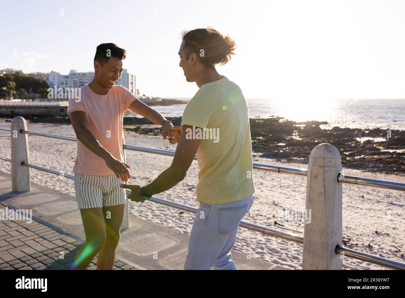 Glückliches birassisches, schwules Paar, das Spaß hat, auf der Promenade am Meer zu tanzen Stockfoto