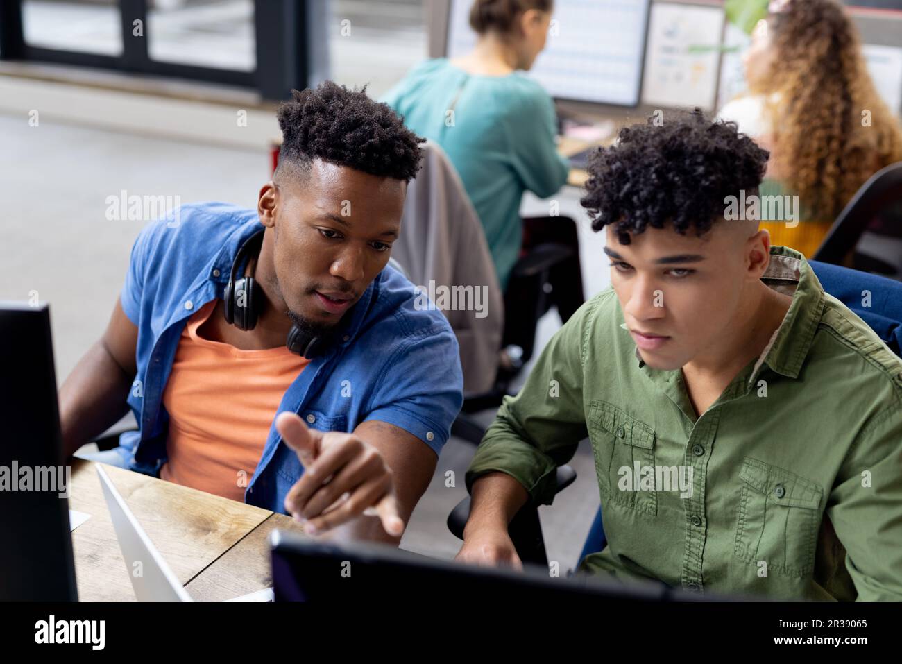 Vielbeschäftigte Geschäftsleute an Schreibtischen, die Computer benutzen und sich in kreativen Büros unterhalten, unverändert Stockfoto