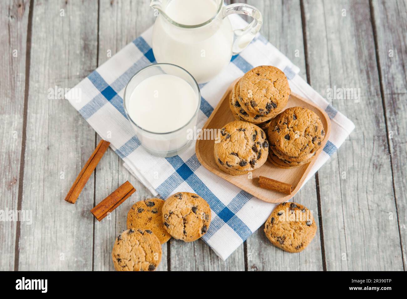 Milch in einem Glas und einer Kanne, mit Schokoladenkeksen und Zimtstangen Stockfoto