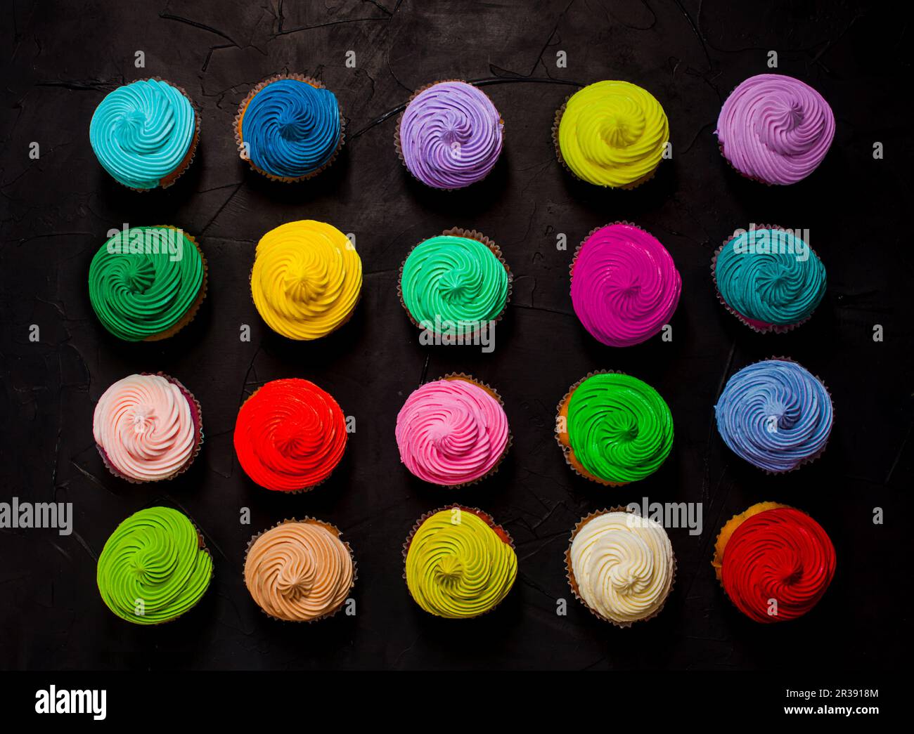 Bunte Regenbogen-Cupcakes in Reihen liegen flach Stockfoto