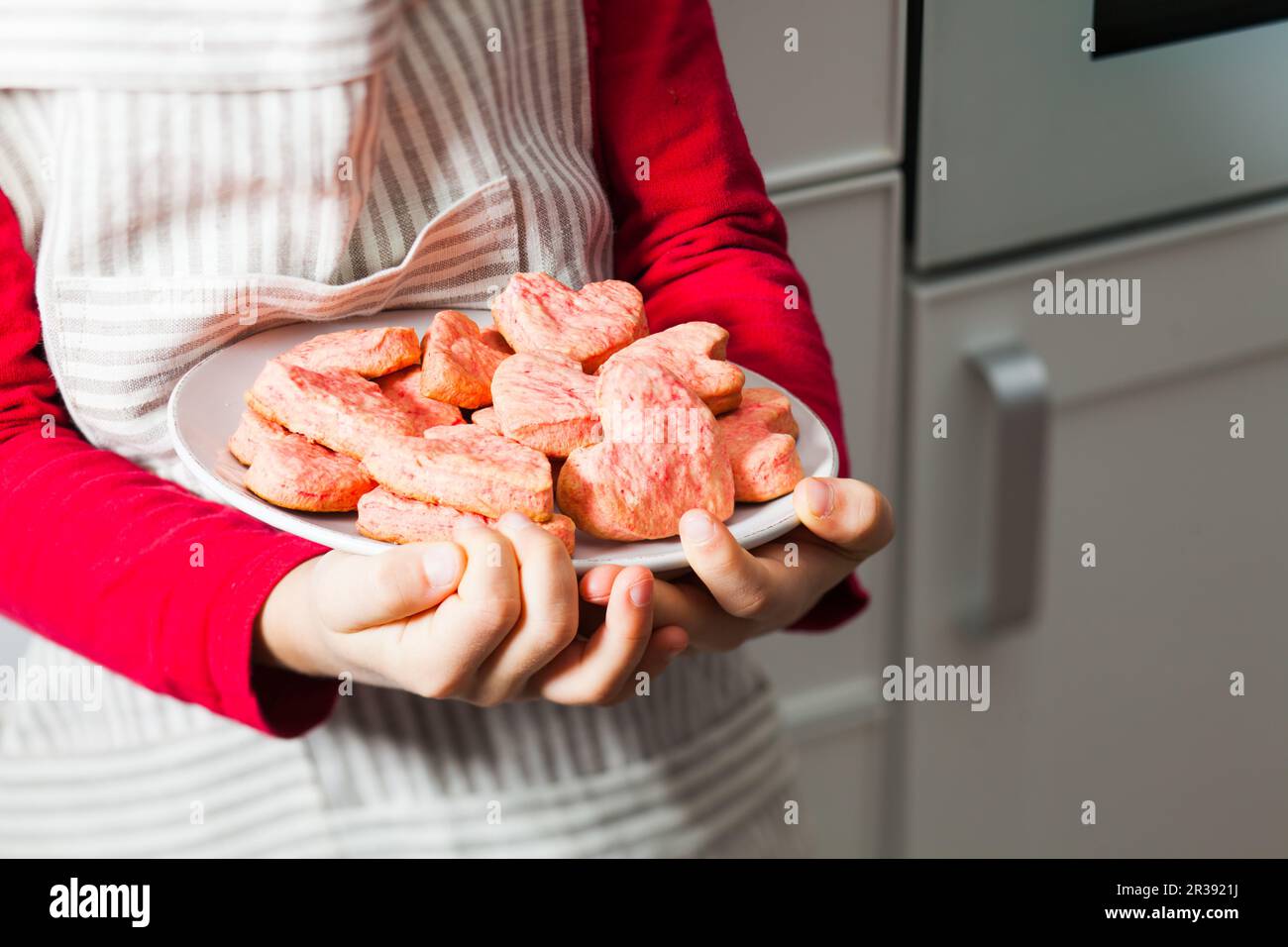 Kinderhände, die rosa Herzkekse auf der Küche halten Stockfoto