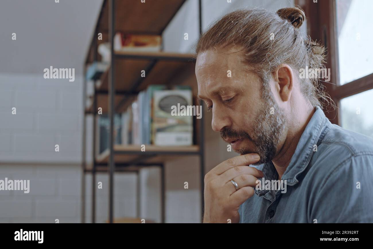 Ein junger besorgter Mann, der ein Notebook benutzt und im Schlafzimmer auf dem Bett sitzt. Stockfoto