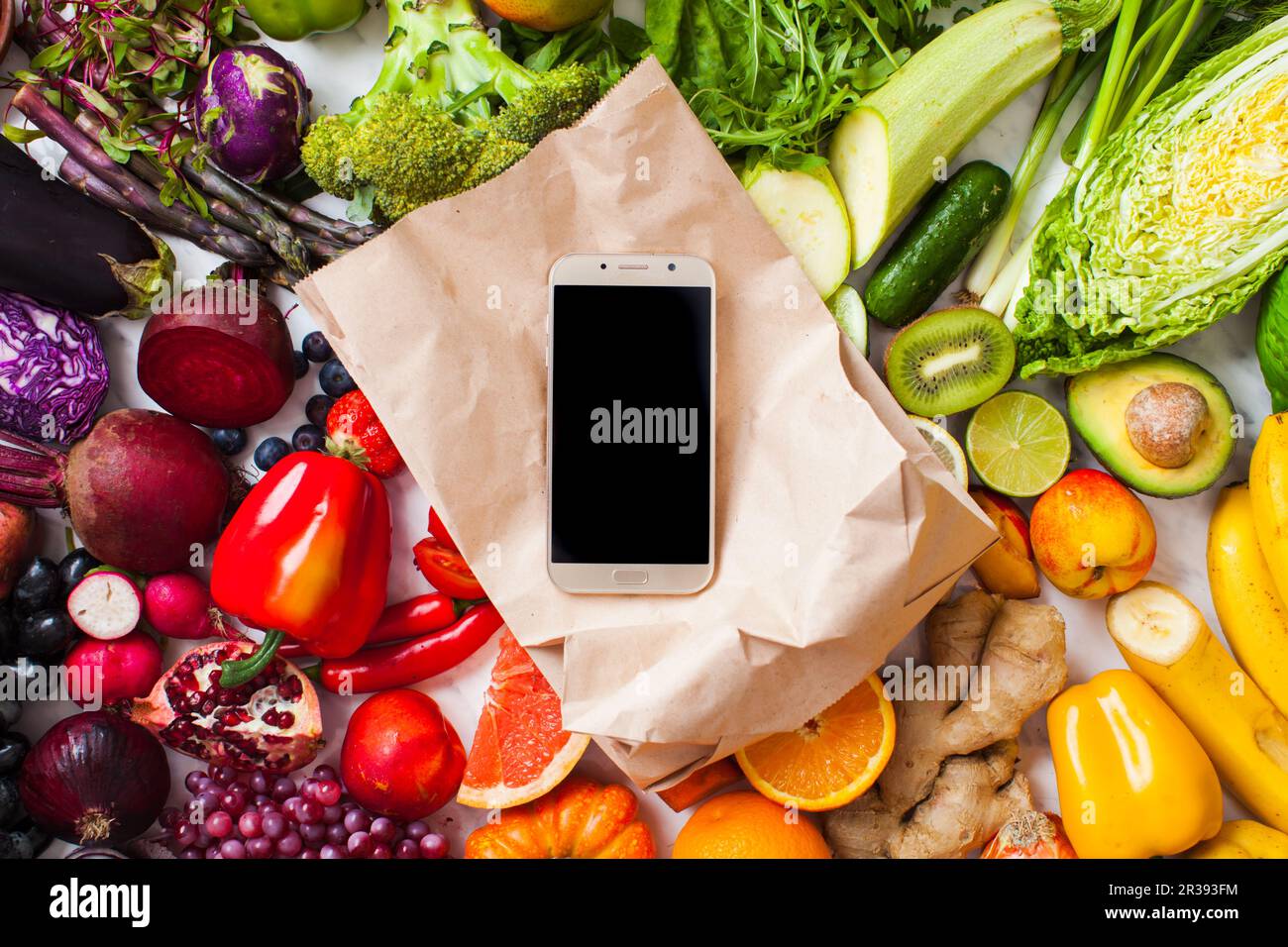 Regenbogenfarbenes Obst und Gemüse auf dem Tisch und Smartphone Stockfoto