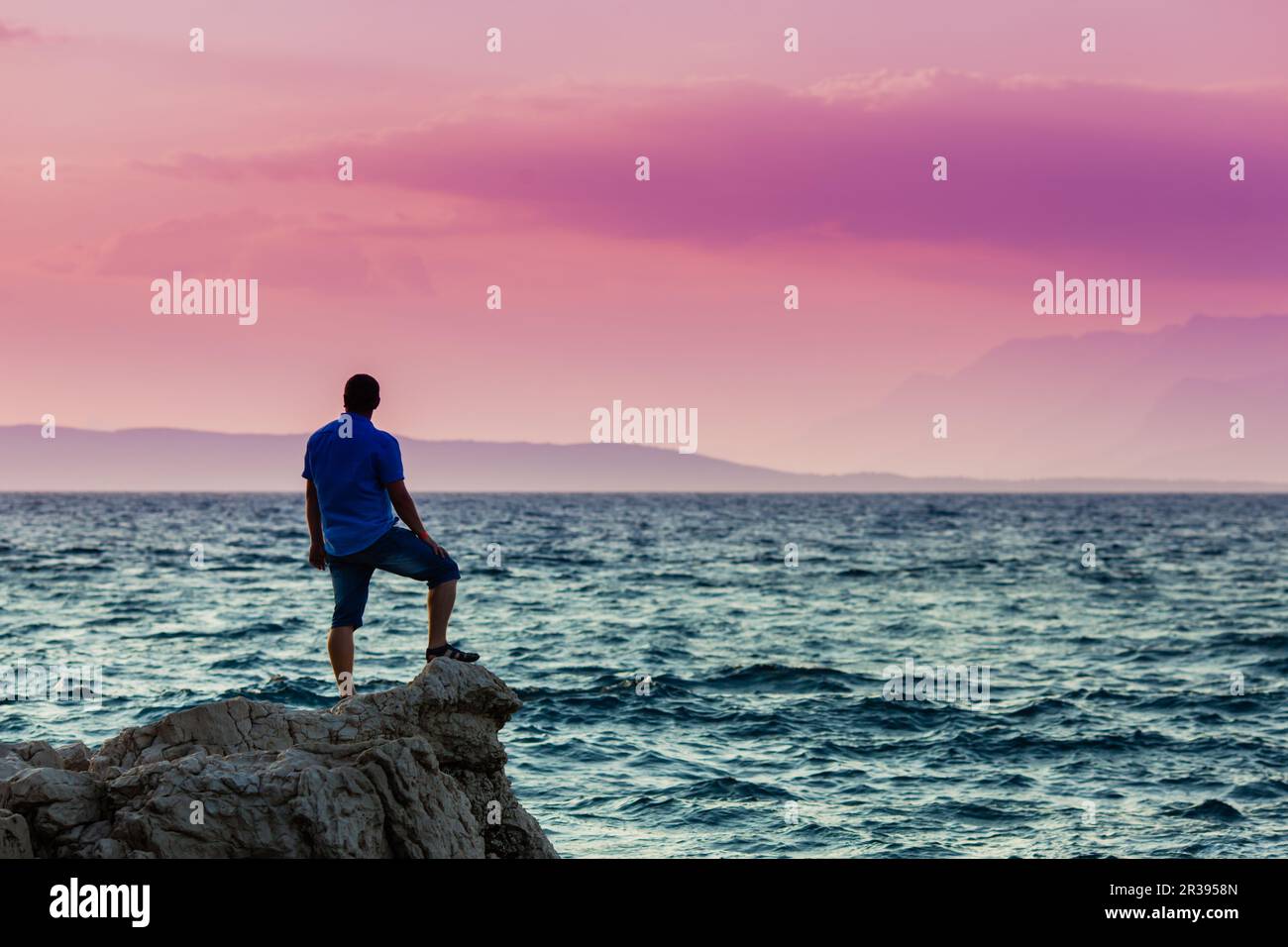 Yung-Mann, der auf einem Felsen steht und den Sonnenuntergang sieht Stockfoto