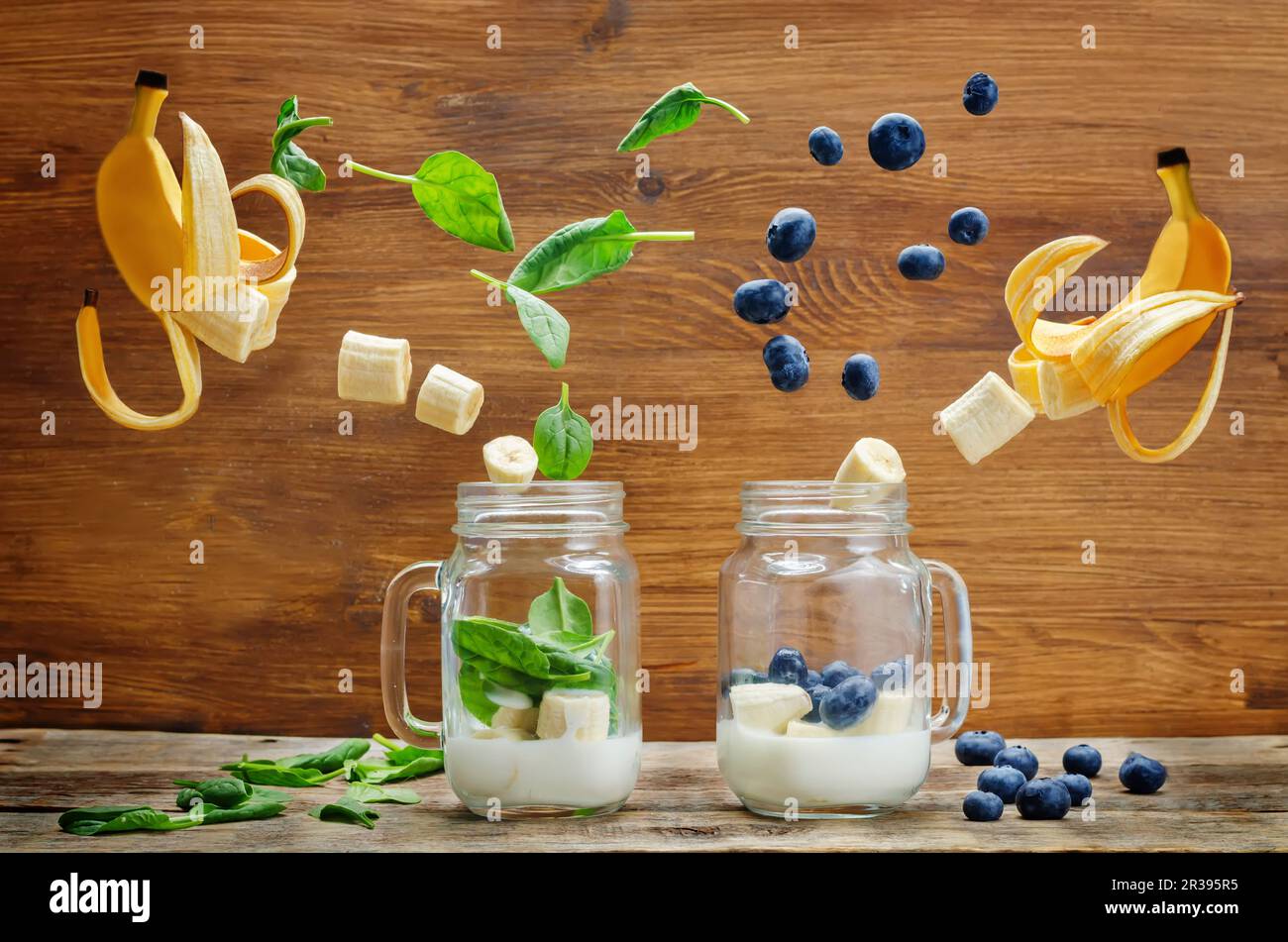 Spinatbananen- und Blaubeerbananen-Smoothie mit fliegenden Scheiben auf Holzhintergrund Stockfoto