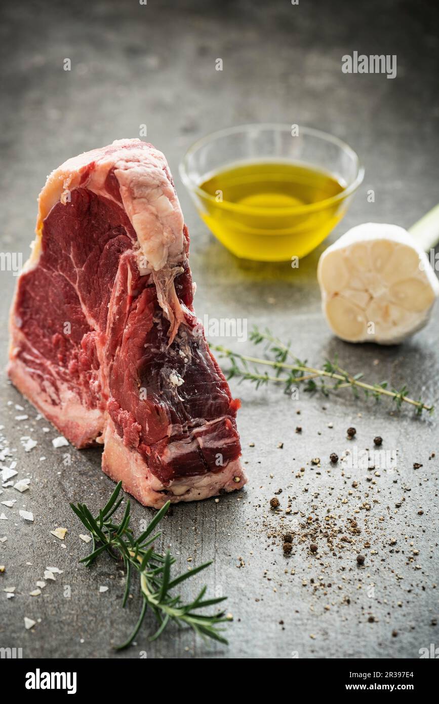 Rohes Porterhouse-Steak mit Kräuterzweigen, Pfeffer, Meersalz, Knoblauch und Olivenöl Stockfoto