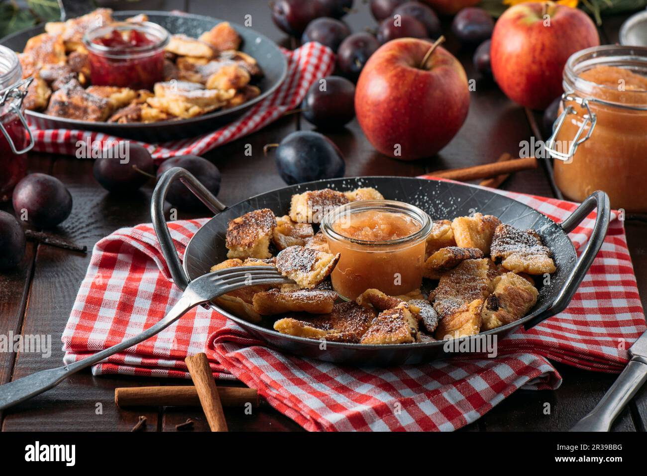 Bohemian Kaiserschmarrn mit Apfelmus und gebratenen Pflaumen in einer gusseisernen Pfanne auf einem rot-weißen Tuch Stockfoto