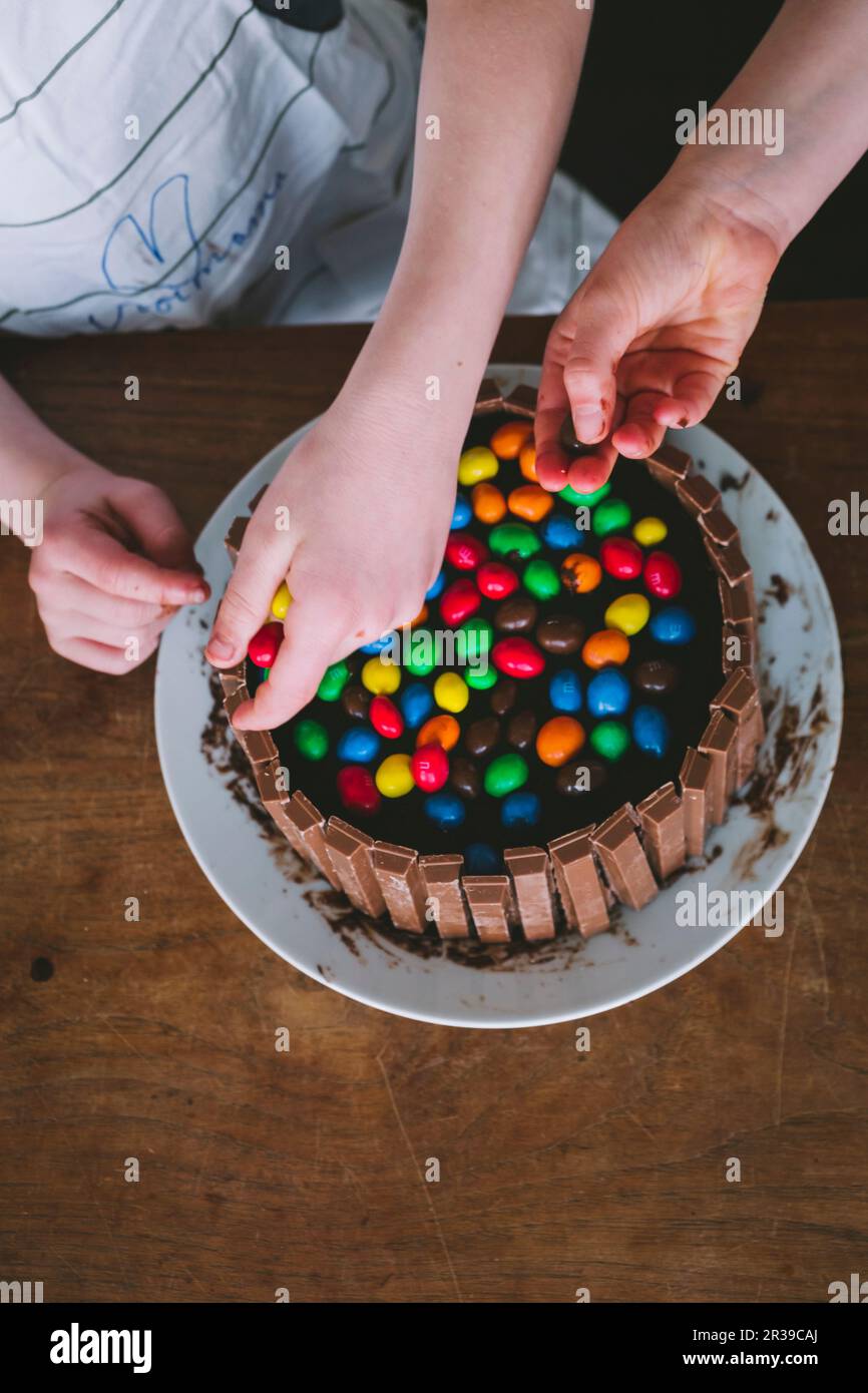 Kinderhände dekorieren einen Kuchen mit bunten Süßigkeiten Stockfoto