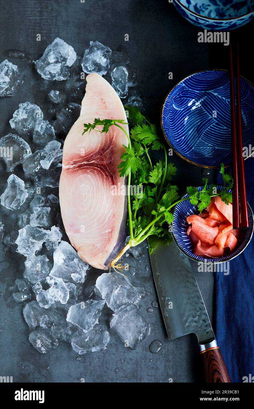 Schwertfischsteak auf Eis neben Koriander, einem Messer und einer orientalischen Schüssel Stockfoto