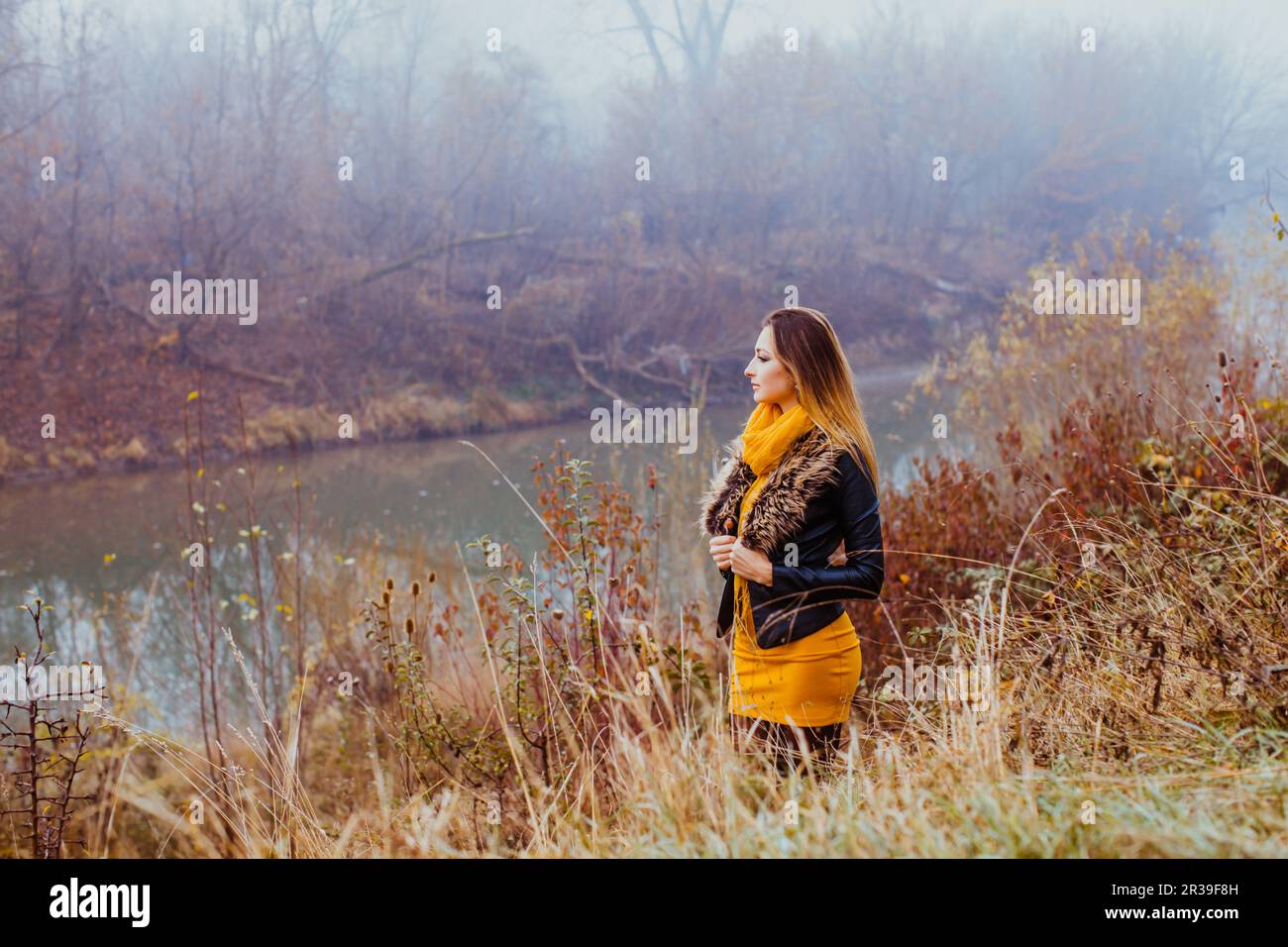 Junge schöne Frau in stilvoller Kleidung, die im Herbst einen Blick auf den Fluss hat Stockfoto