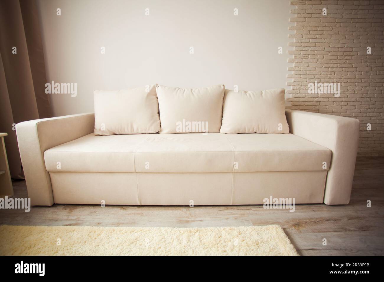 Beige Sofa gegen weiße Ziegelwand mit Kopierraum. Stockfoto