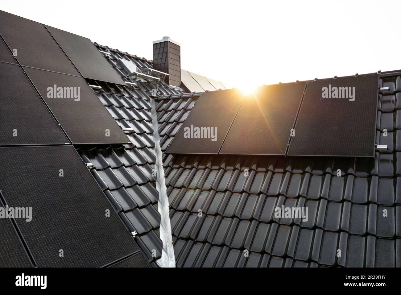 Sonnenkollektoren auf einem dunklen Ziegeldach, die bei Sonnenaufgang mit einer Lichtscheibe erfasst wurden Stockfoto