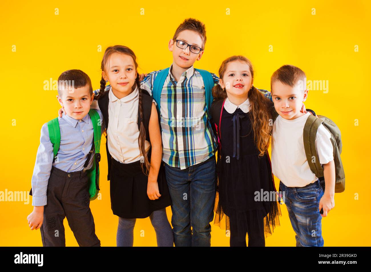 Intelligente Schüler lächeln und schauen auf die Kamera über gelbem Hintergrund. Fröhliche Kinder in Schuluniform mit Rucksäcken Stockfoto