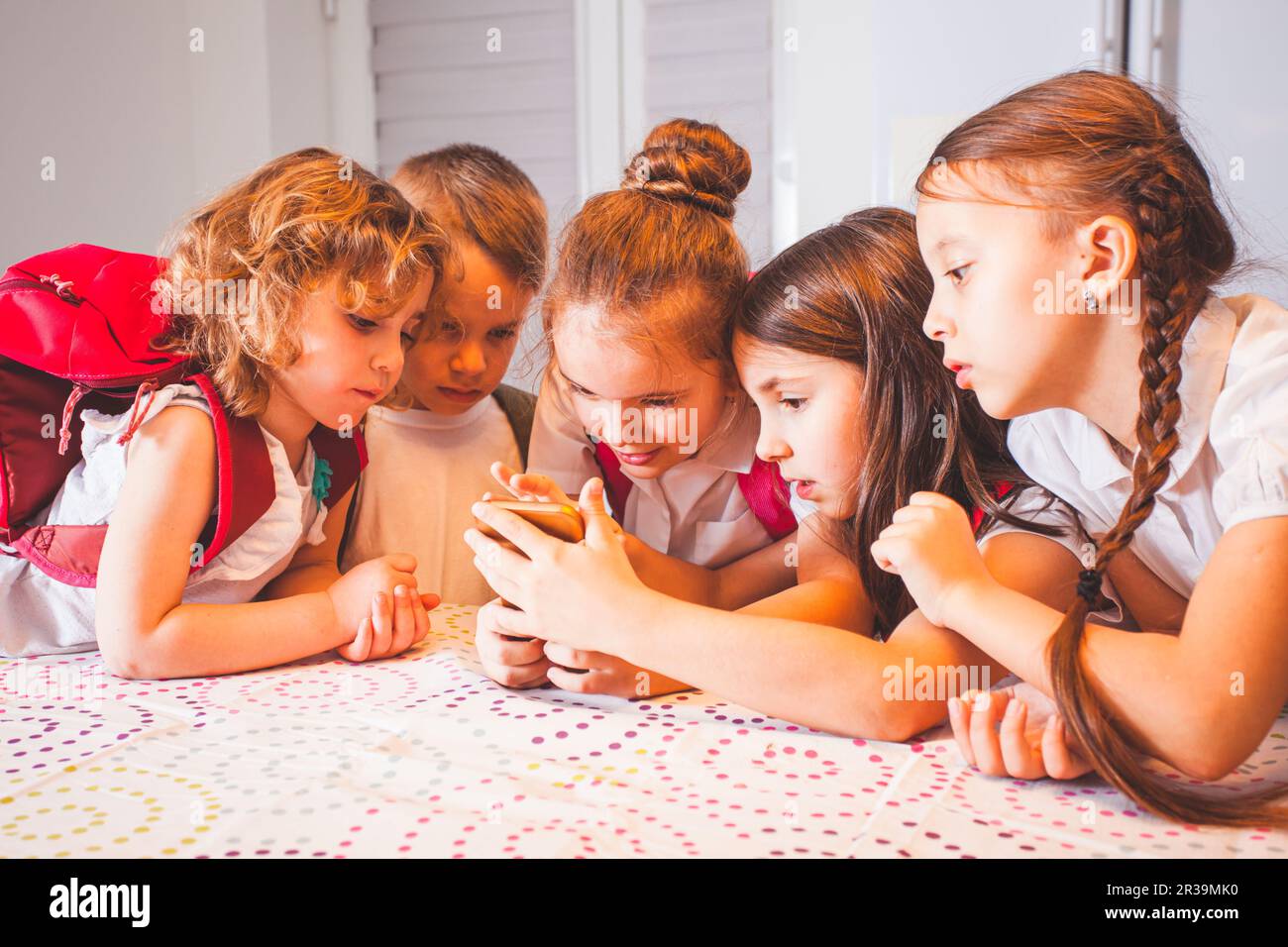 Eine Gruppe von Schulkindern mit Smartphone, die Spaß am Pausenbetrieb im Klassenzimmer haben Stockfoto
