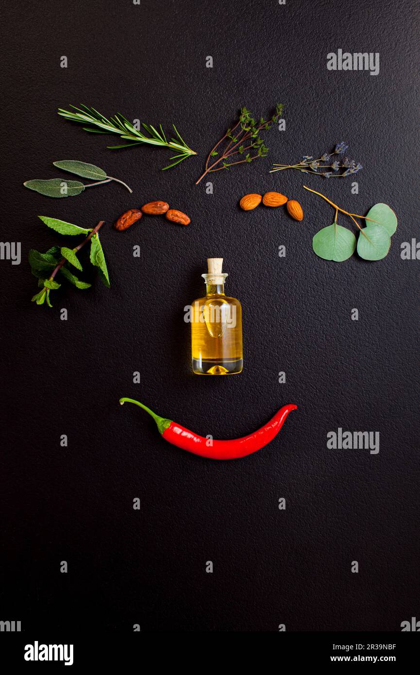 Lächelndes Gesicht aus Kräutern und Flasche ätherisches Öl auf schwarzem Hintergrund, Draufsicht, flacher Lay Stockfoto
