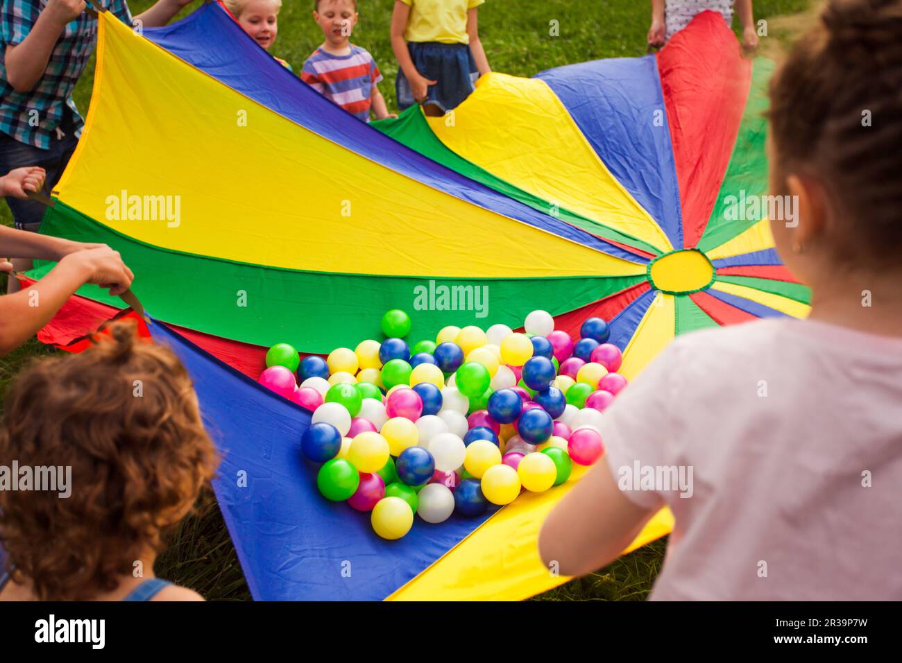 Glückliche Kinder, die mit einem Regenbogenschirm voller Bälle wedeln Stockfoto