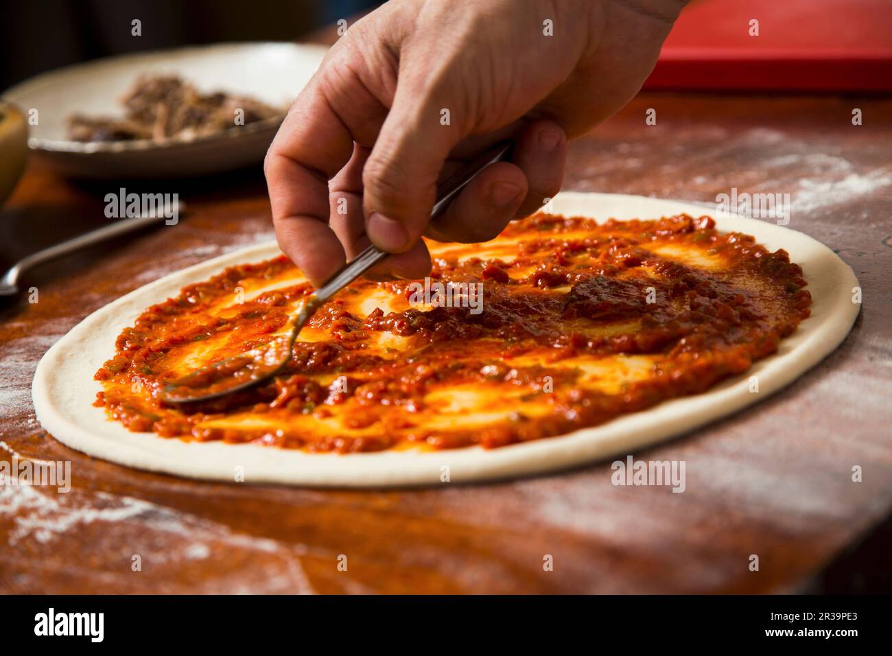 Tomatensoße zur Pizza hinzufügen Stockfoto