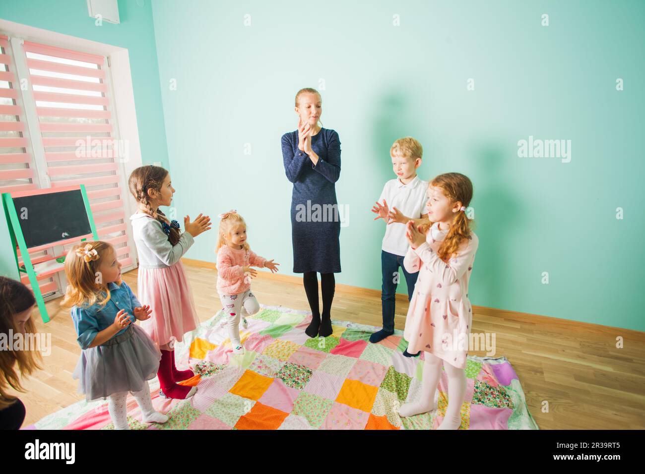 Kinder singen gemeinsam ein Lied mit einem Lehrer. Kinder in einer Kinderkrippe. Stockfoto