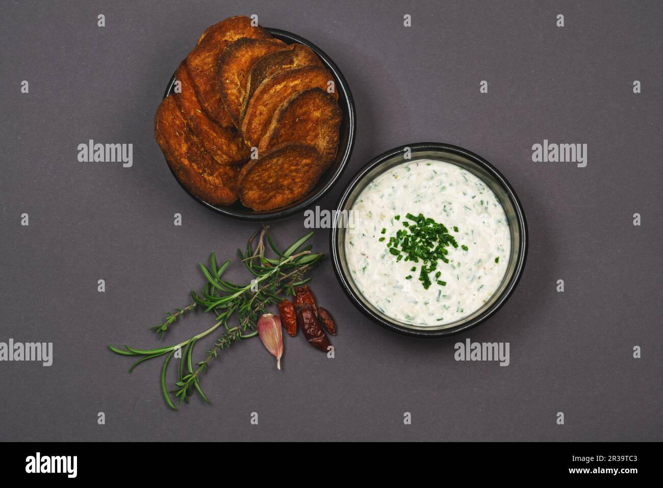 Atemberaubender Blick auf scharfe Süßkartoffelchips mit Chili, Rosmarin und Thymian sowie Joghurt, Knoblauch-Schnittlauch-Dip-Sauce in schwarzen Schüsseln Stockfoto