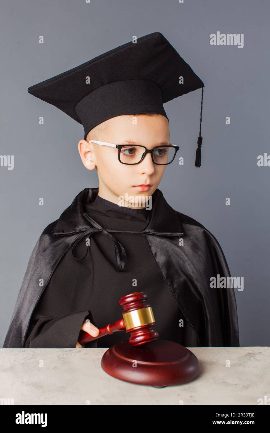 Porträt eines ernsthaften, intelligenten Kindes in der Abschlusskappe, das im Richter spielt. Stockfoto