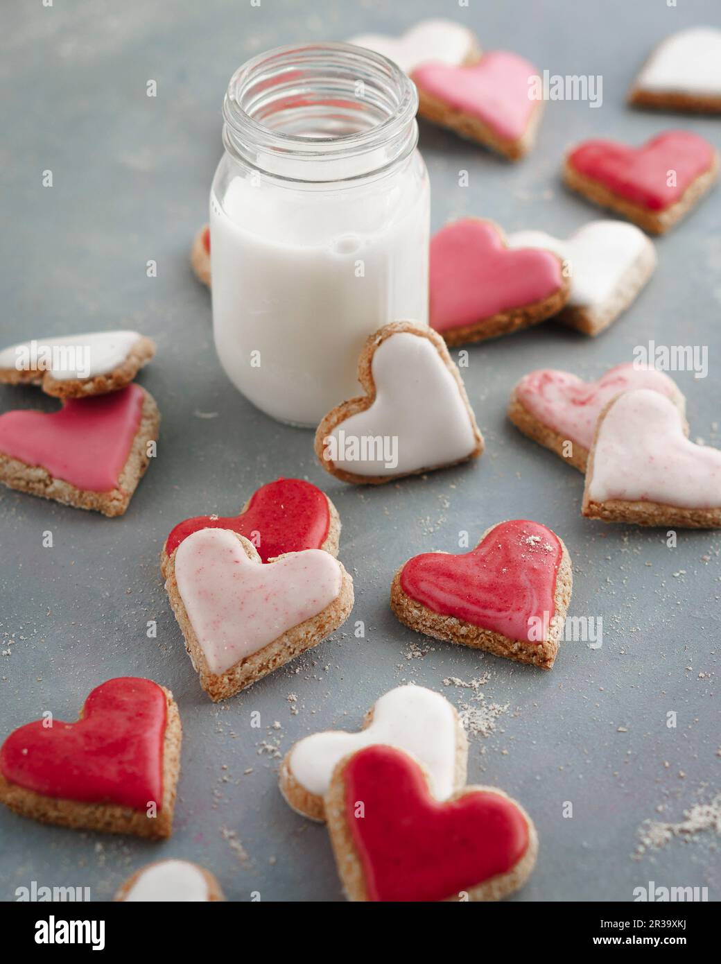 Rosafarbene, rote und weiße herzförmige Kekse mit einem Glas Milch Stockfoto