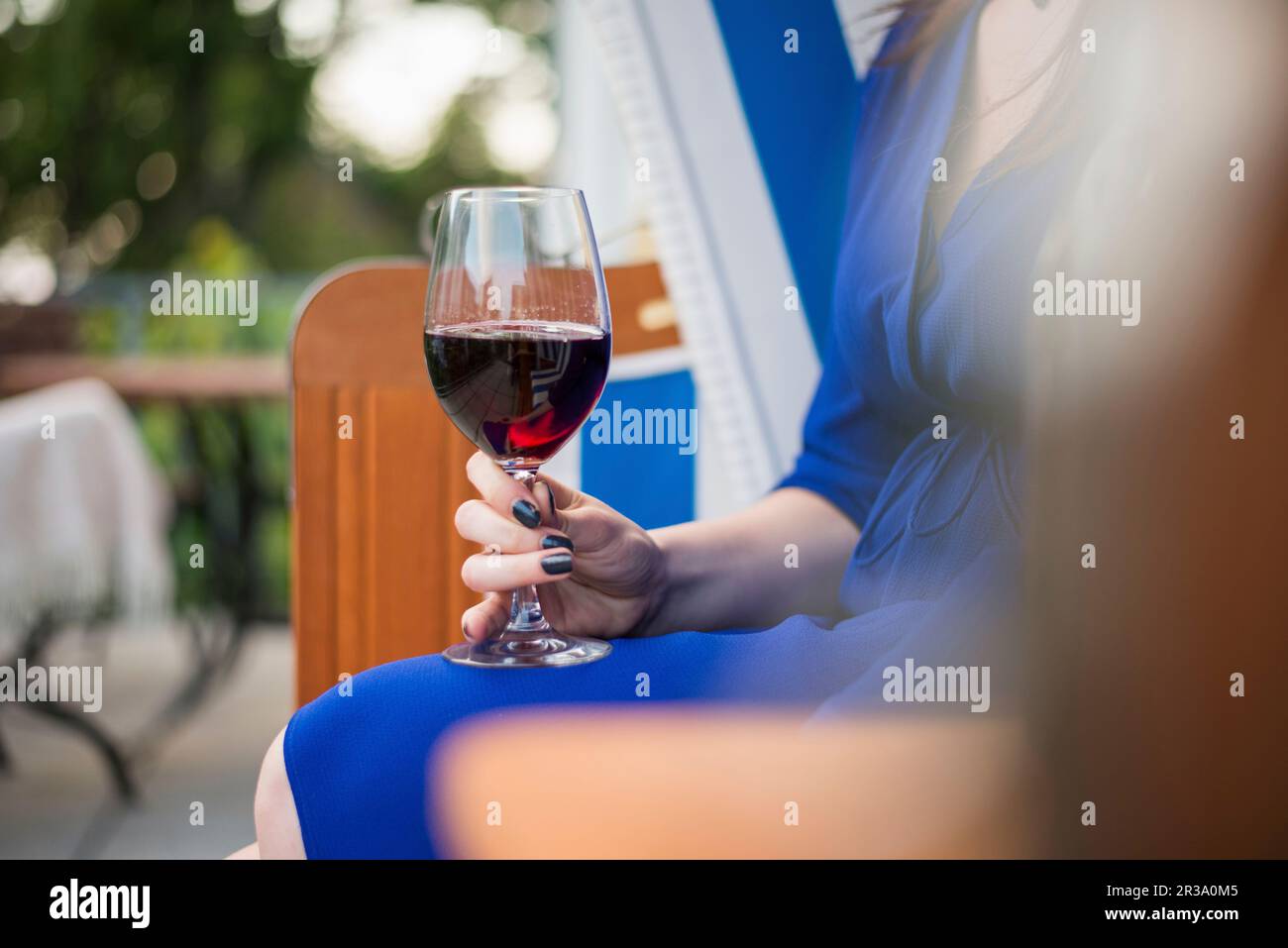 Eine Frau, die mit einem Glas Rotwein auf einem Liegestuhl sitzt Stockfoto